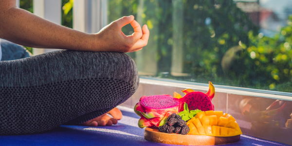 woman sitting cross legged in front of window meditating with plate of fruit next to her