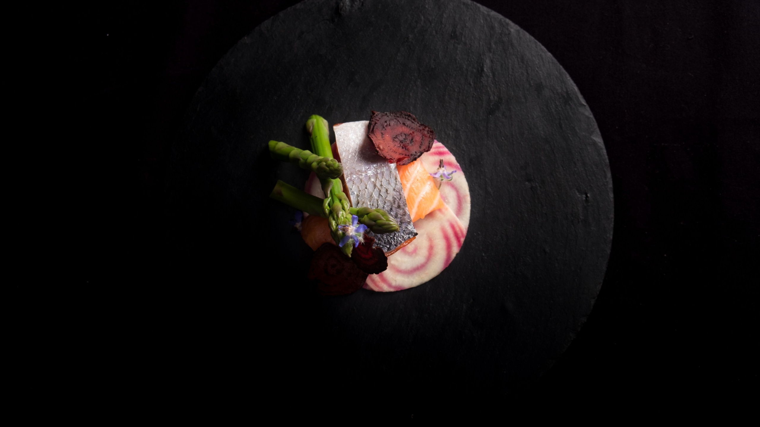 vibrant food on a black plate surrounded by darkness